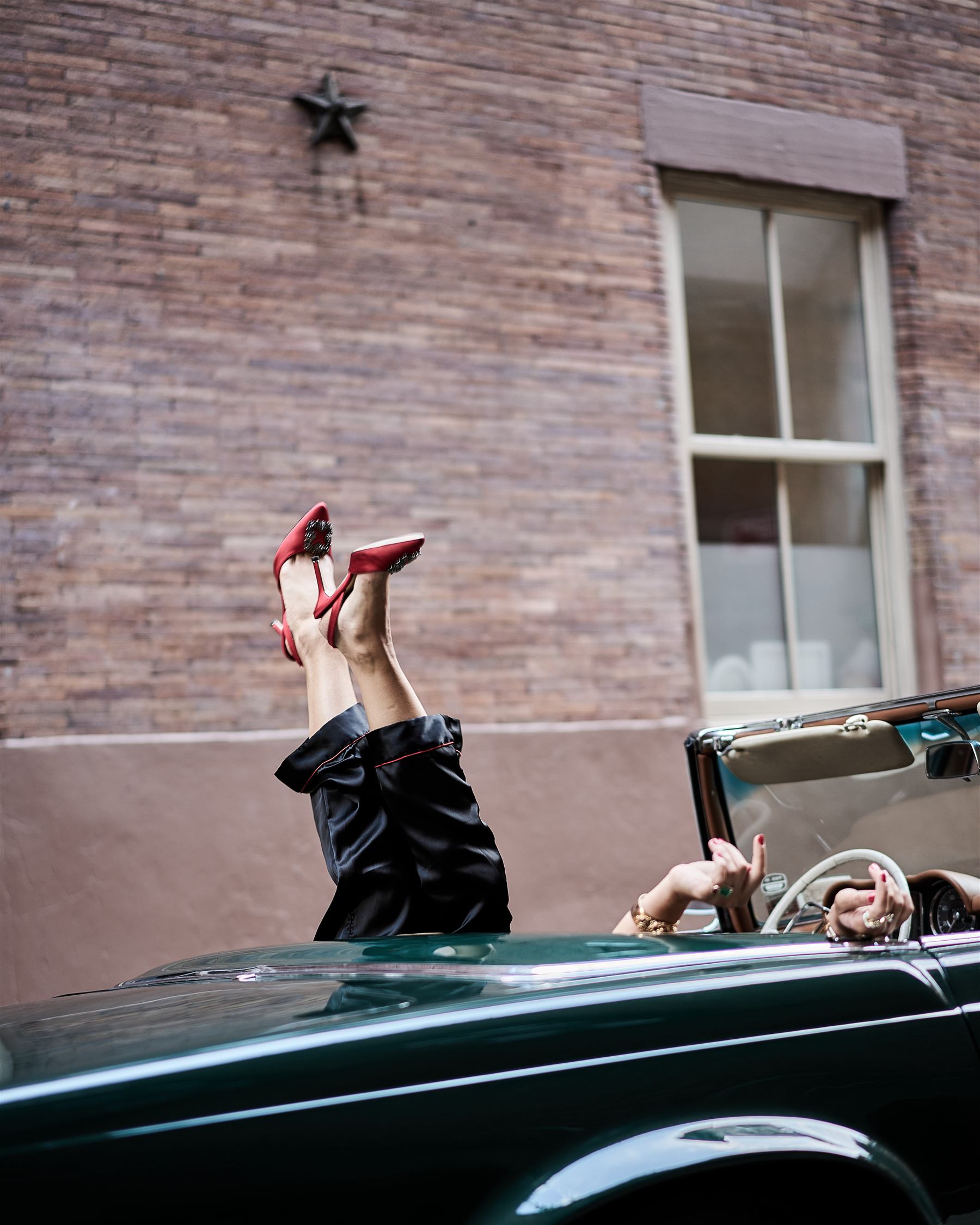 Red satin heels kicked up over the door of the vintage green Mercedes, against a brick wall