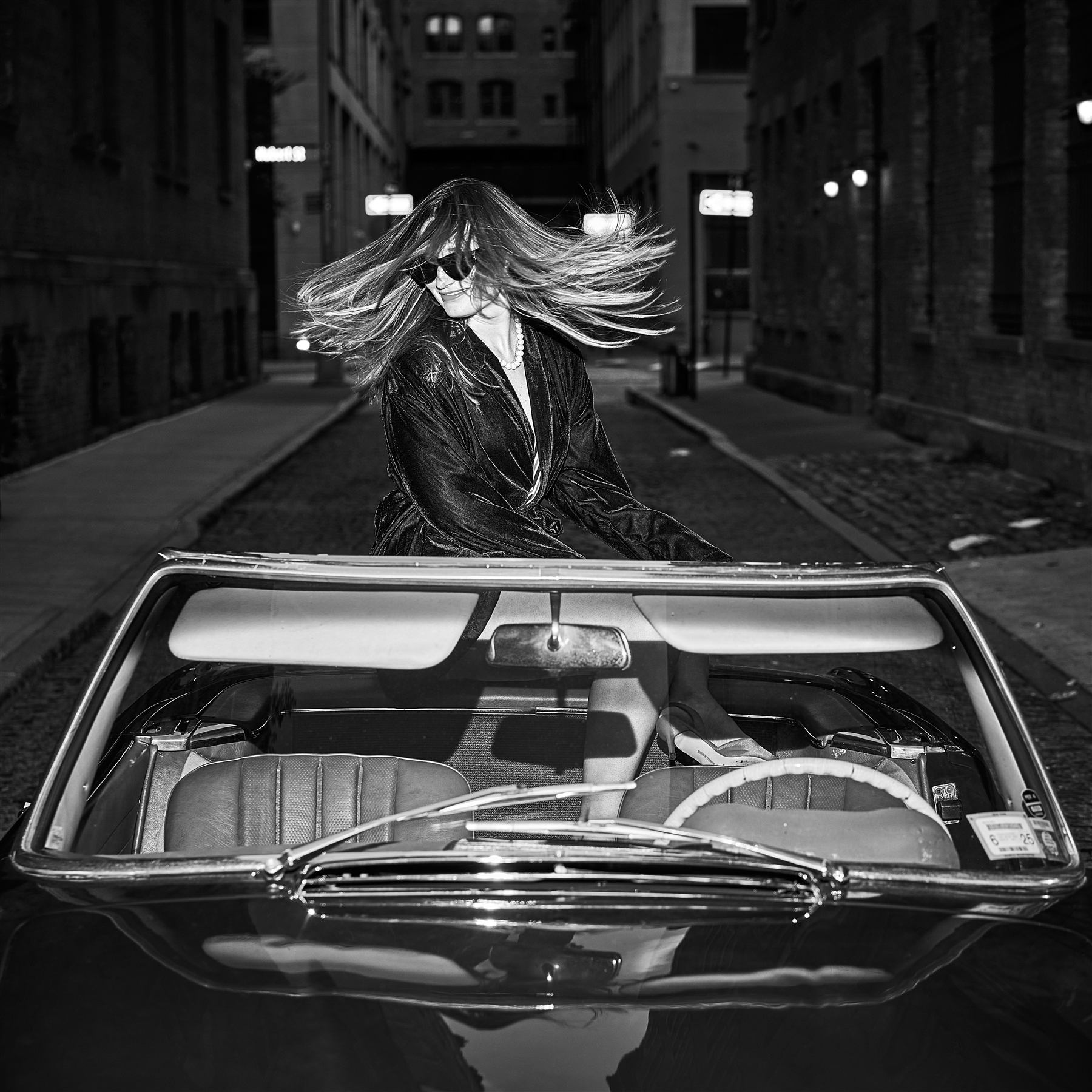 A model with wind-swept hair at night behind the vintage Mercedes