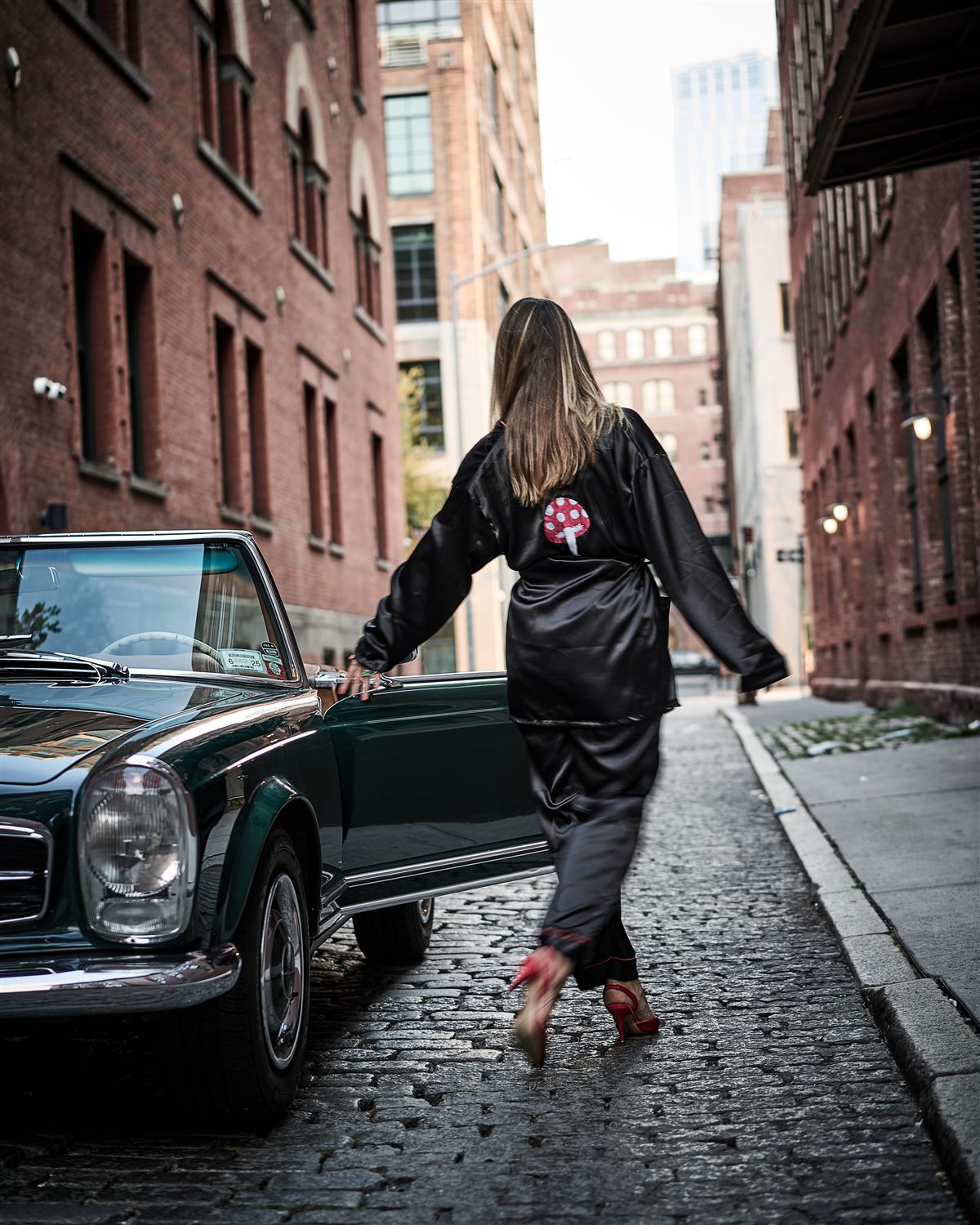 A model walking a New York street beside the vintage green Mercedes in evening light