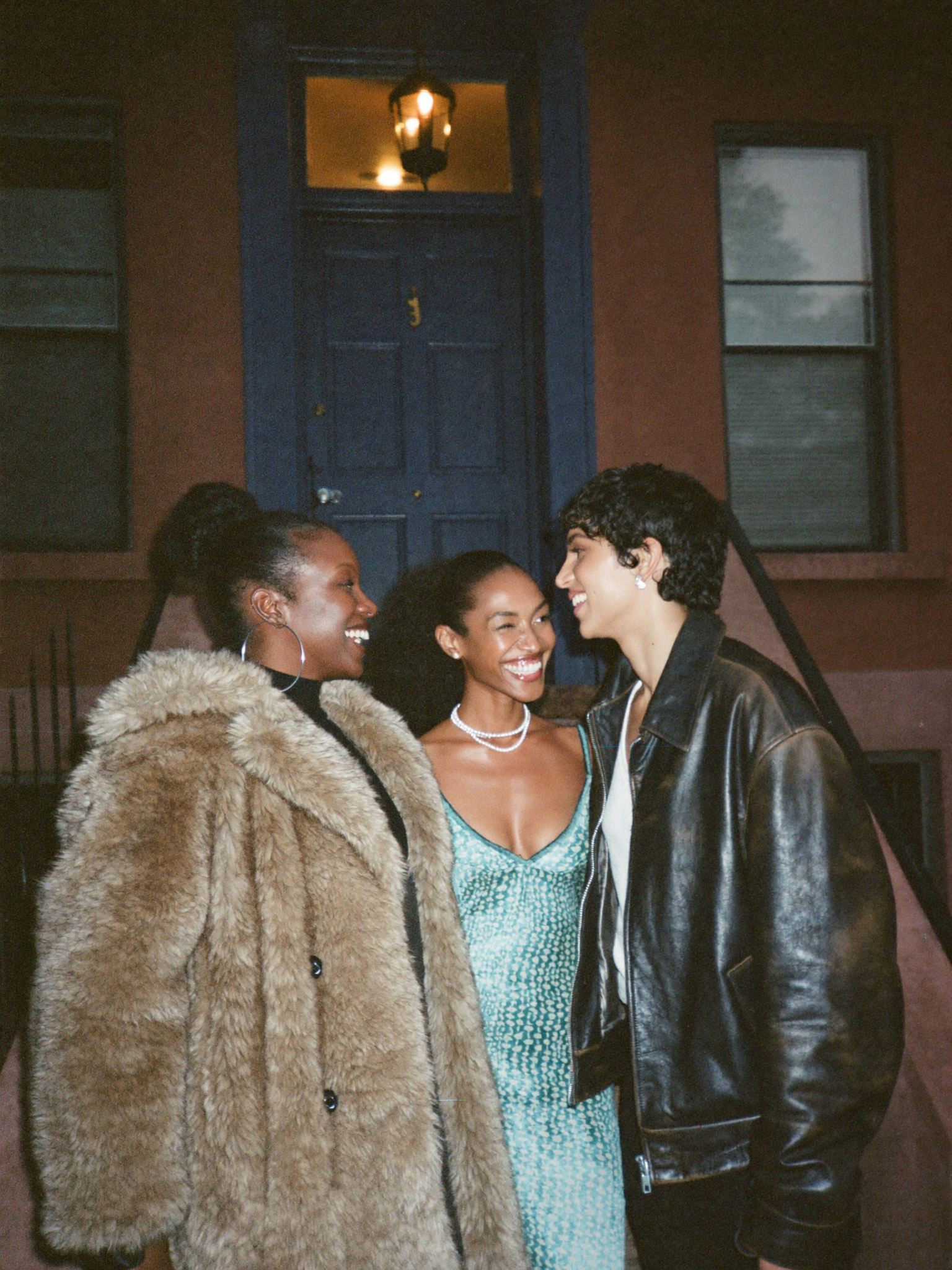 Three friends laughing together on a brownstone stoop at night