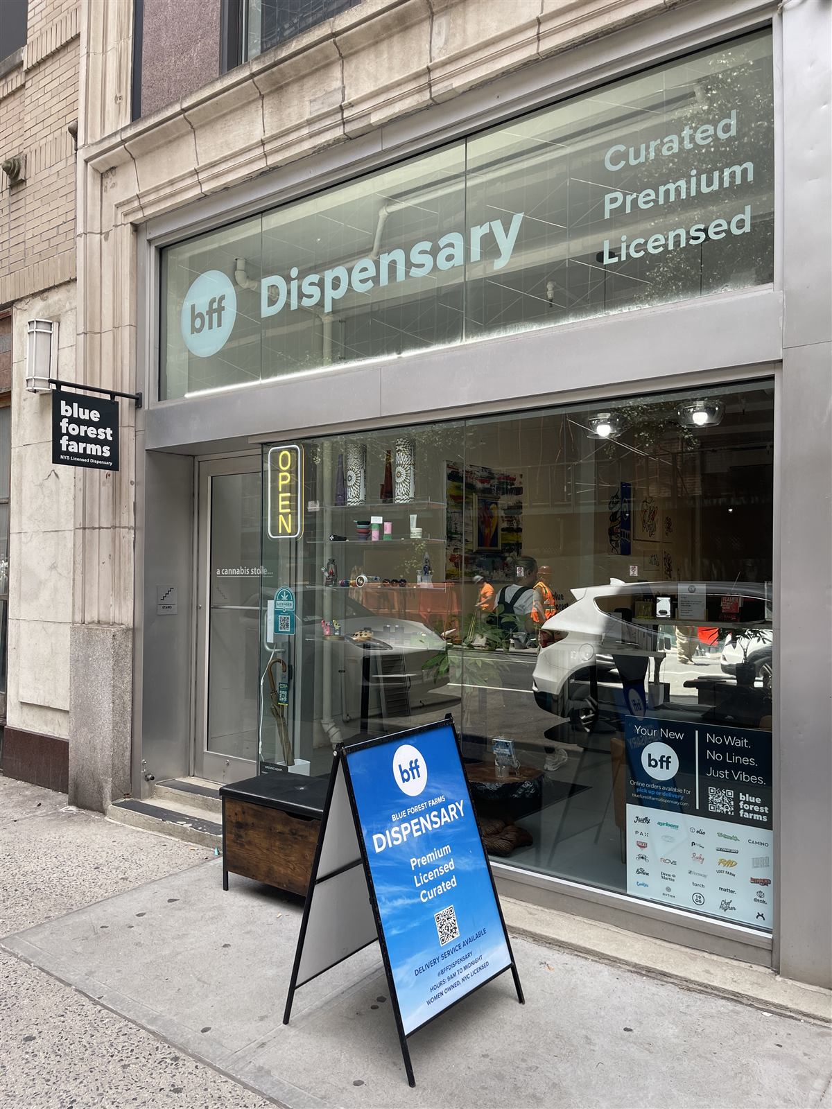 The real BFF Dispensary storefront at 122 E 25th Street — glass facade reading 'bff Dispensary · Curated · Premium · Licensed', with the blue forest farms blade sign and blue A-frame out front